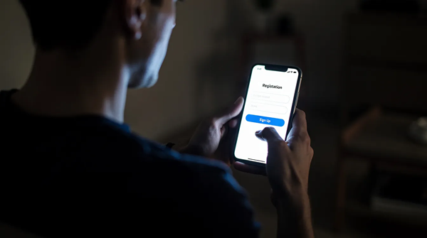 薄暗い部屋で、スマートフォンを持つ人物が画面に光る登録フォームを表示しています。この画像は、オンラインカジノ「ステ ルス ベット」の登録プロセスを示しており、入金不要ボーナスを受け取るための手続きを連想させます。